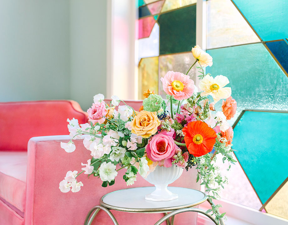 beautiful floral arrangement on a side table next to a pink sofa and stainglass window